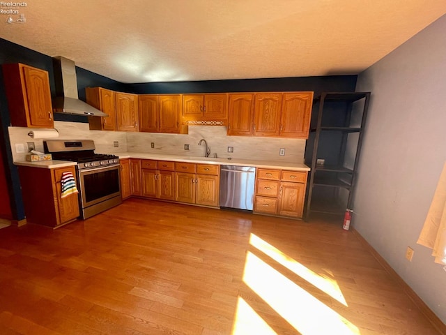 kitchen featuring tasteful backsplash, light wood-type flooring, light countertops, appliances with stainless steel finishes, and wall chimney exhaust hood