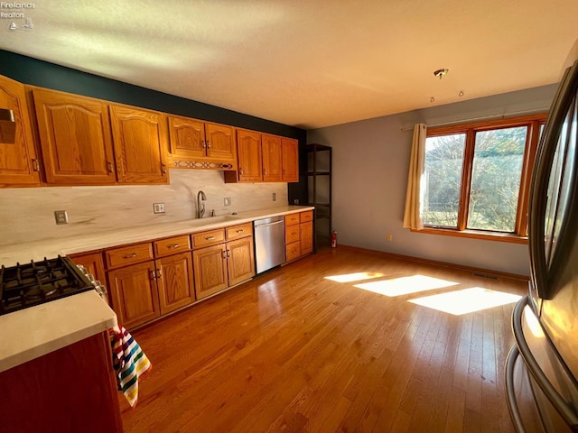 kitchen with light wood-type flooring, a sink, stainless steel appliances, brown cabinetry, and light countertops