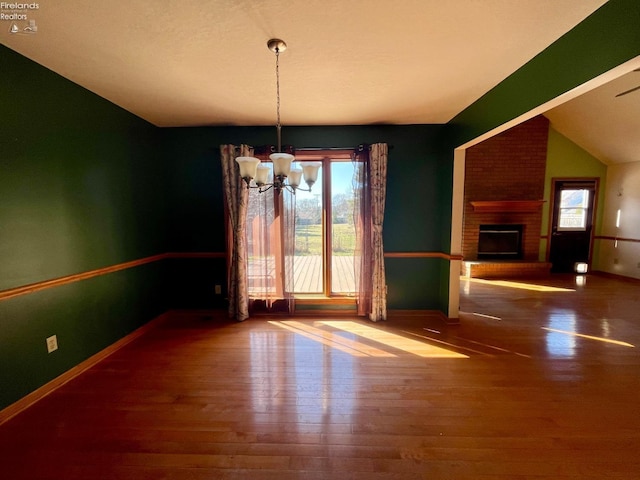 unfurnished dining area featuring a healthy amount of sunlight, a brick fireplace, an inviting chandelier, and wood finished floors