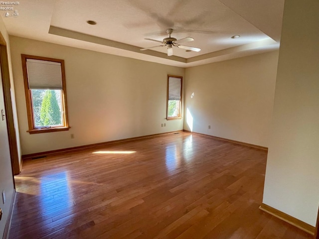 unfurnished room featuring a tray ceiling, baseboards, wood finished floors, and a ceiling fan