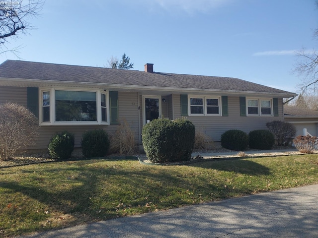 ranch-style home with a chimney, a front yard, and a shingled roof