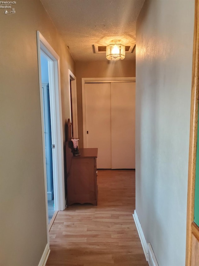 hallway featuring a textured ceiling, light wood-type flooring, and baseboards