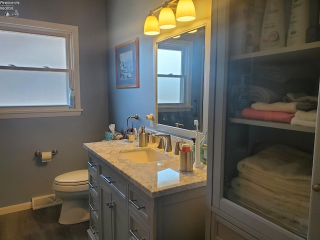 half bathroom with toilet, plenty of natural light, wood finished floors, and visible vents