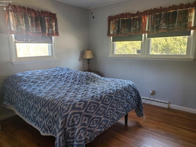 bedroom with multiple windows, hardwood / wood-style flooring, baseboards, and a baseboard radiator