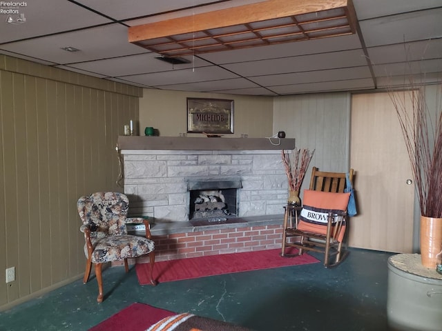 below grade area with a drop ceiling, a stone fireplace, and wooden walls