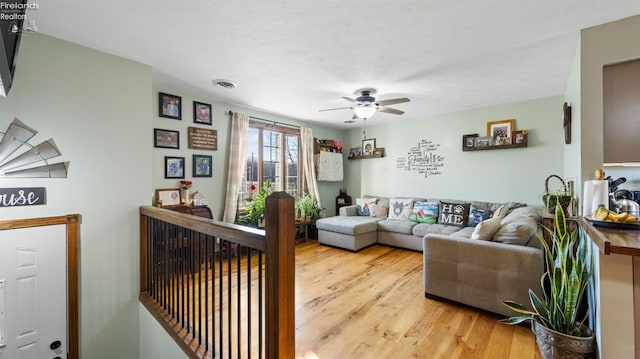 living area featuring visible vents, a textured ceiling, a ceiling fan, and light wood-style floors
