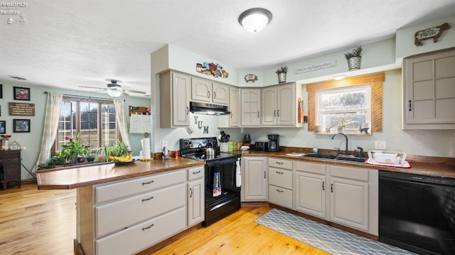 kitchen featuring light wood-type flooring, black appliances, under cabinet range hood, a sink, and a peninsula