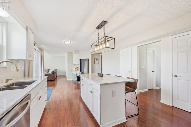 kitchen featuring a sink, a kitchen breakfast bar, stainless steel dishwasher, white cabinets, and dark wood-style flooring