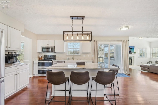 kitchen with a sink, open floor plan, a breakfast bar, stainless steel appliances, and dark wood-style flooring