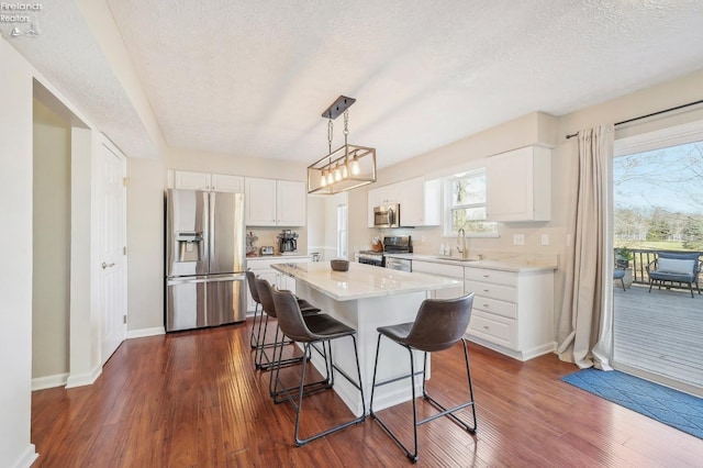 kitchen with appliances with stainless steel finishes, white cabinetry, a kitchen bar, and dark wood-type flooring