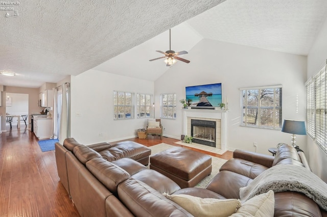 living room with a wealth of natural light, a tile fireplace, a ceiling fan, and wood finished floors