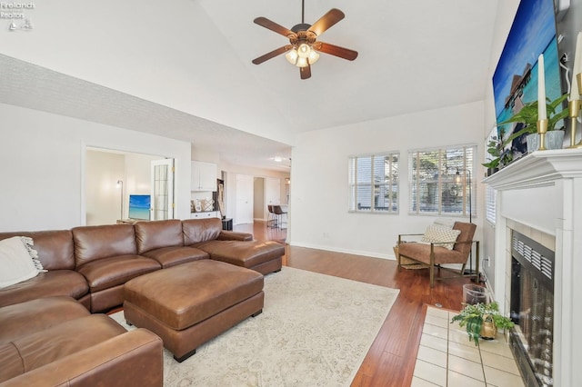 living room featuring wood finished floors, baseboards, high vaulted ceiling, a fireplace, and ceiling fan