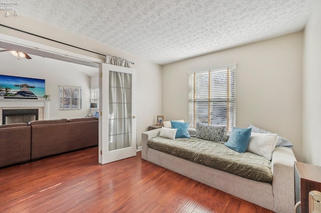 living room featuring ceiling fan, wood finished floors, a tile fireplace, and a textured ceiling