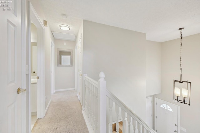 hall with an upstairs landing, light colored carpet, a textured ceiling, and baseboards