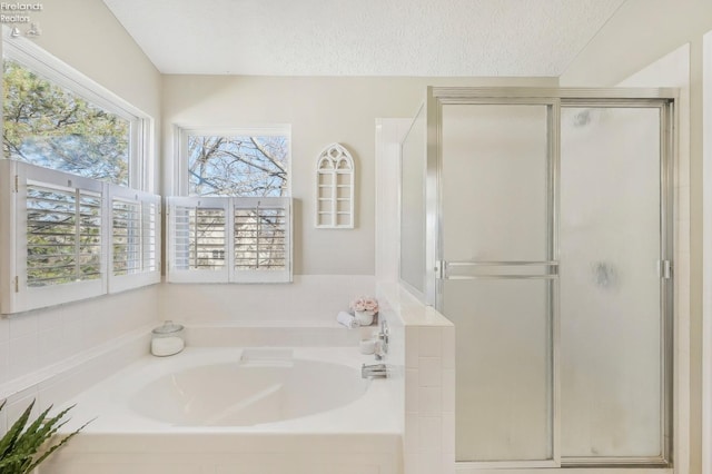 full bath with a stall shower, a textured ceiling, and a garden tub