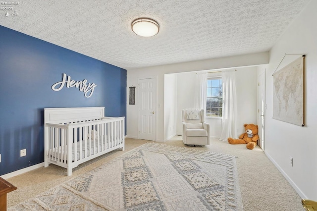 bedroom with baseboards, a crib, a textured ceiling, and carpet