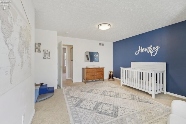 bedroom featuring visible vents, a crib, a textured ceiling, carpet floors, and baseboards