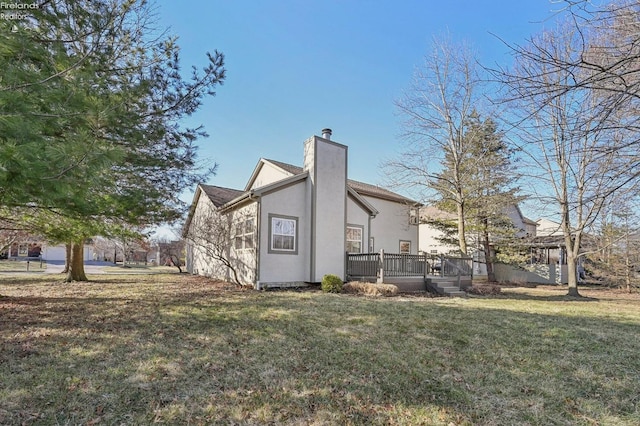 exterior space with a chimney, a lawn, a wooden deck, and stucco siding