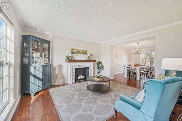 living room with wood finished floors, ornamental molding, a textured ceiling, a brick fireplace, and a chandelier