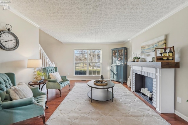 living area featuring ornamental molding, a textured ceiling, wood finished floors, a fireplace, and baseboards