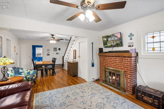 living area featuring stairway, wood finished floors, a ceiling fan, a fireplace, and ornamental molding