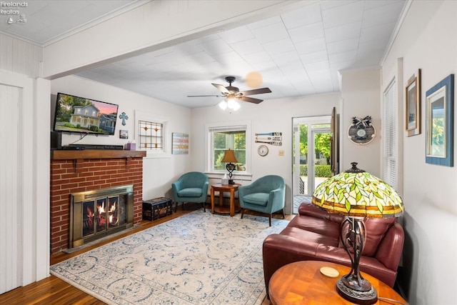 living room featuring ceiling fan, a brick fireplace, wood finished floors, and crown molding