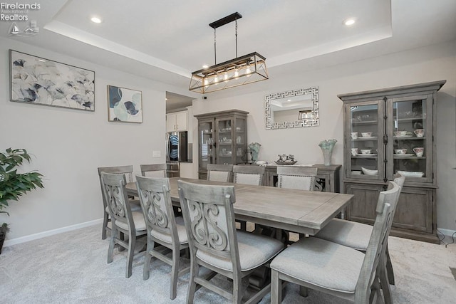 dining space with a tray ceiling, baseboards, and light colored carpet