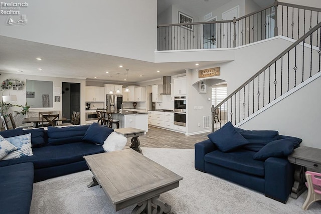 living area with visible vents, stairs, recessed lighting, a high ceiling, and light wood-style floors