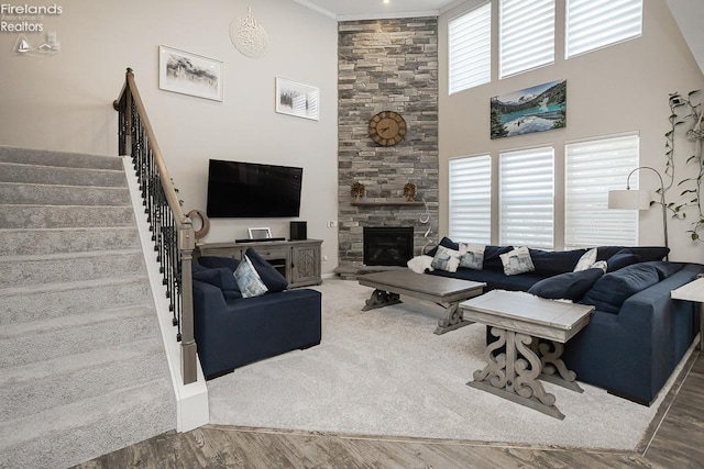 living area with a stone fireplace, stairway, a high ceiling, and wood finished floors