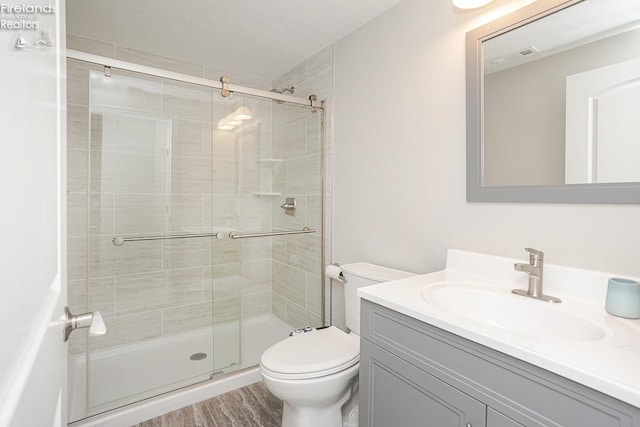 bathroom with visible vents, a shower stall, toilet, wood finished floors, and vanity