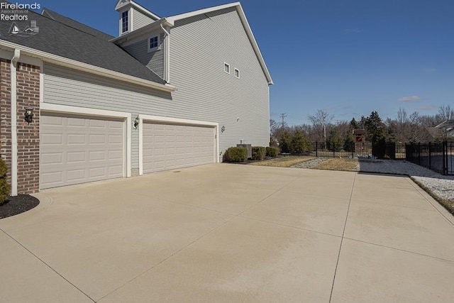 view of property exterior featuring a garage, roof with shingles, driveway, and fence