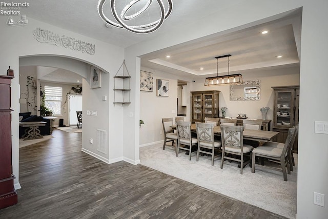 dining space with visible vents, a tray ceiling, recessed lighting, arched walkways, and dark wood-style flooring