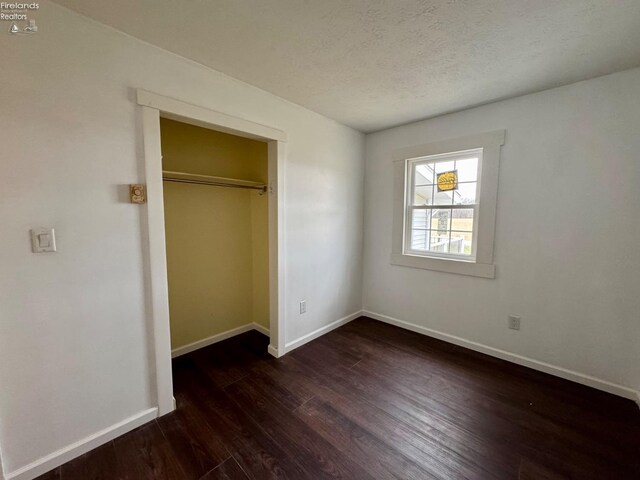 unfurnished bedroom featuring a textured ceiling, baseboards, and wood finished floors
