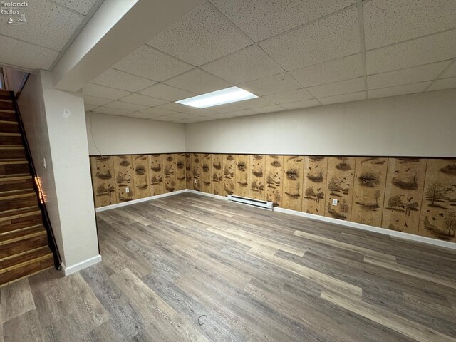 finished basement featuring visible vents, baseboards, a drop ceiling, stairs, and wood finished floors