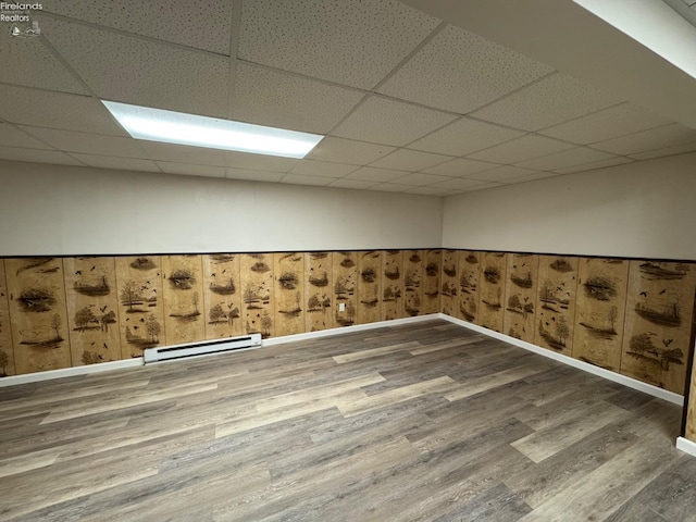 empty room featuring a drop ceiling, a baseboard radiator, and wood finished floors