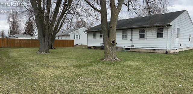 rear view of property with crawl space, fence, and a lawn