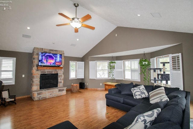 living room featuring ceiling fan, a stone fireplace, baseboards, and wood finished floors