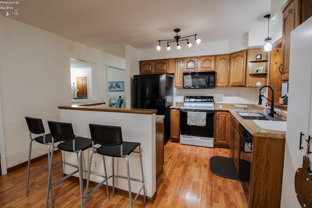 kitchen with range with electric stovetop, a sink, a kitchen bar, brown cabinets, and black microwave