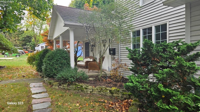 view of side of home with a shingled roof and covered porch