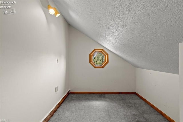 additional living space featuring baseboards, vaulted ceiling, carpet, and a textured ceiling