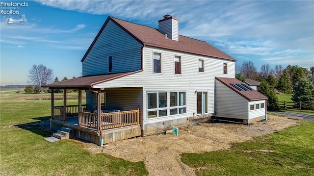 back of house with a chimney, roof with shingles, and a yard