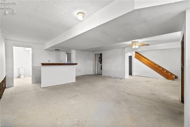 unfurnished living room with a textured ceiling, concrete floors, ceiling fan, and bar