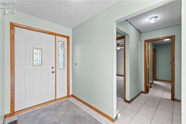 foyer featuring light tile patterned floors, baseboards, ceiling fan, and a textured ceiling