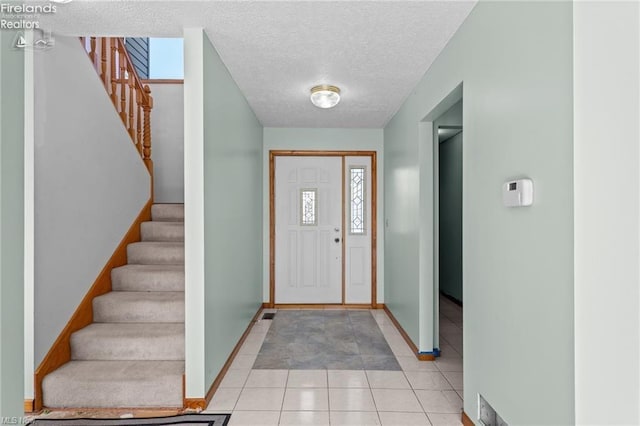 entrance foyer with baseboards, a textured ceiling, stairway, and light tile patterned floors