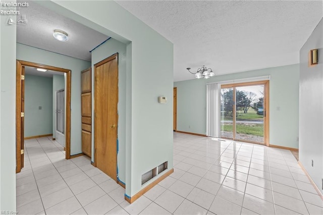 corridor featuring a textured ceiling, a chandelier, baseboards, and light tile patterned floors