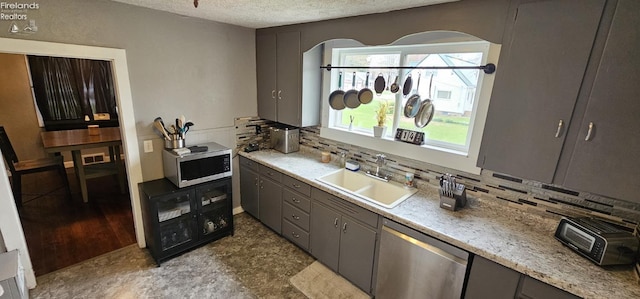 kitchen with a textured ceiling, gray cabinetry, stainless steel appliances, arched walkways, and a sink