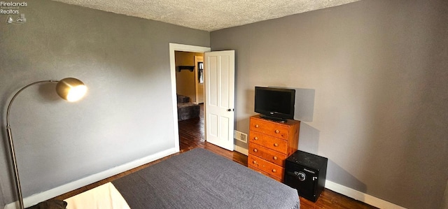 bedroom with a textured ceiling, baseboards, dark wood finished floors, and visible vents
