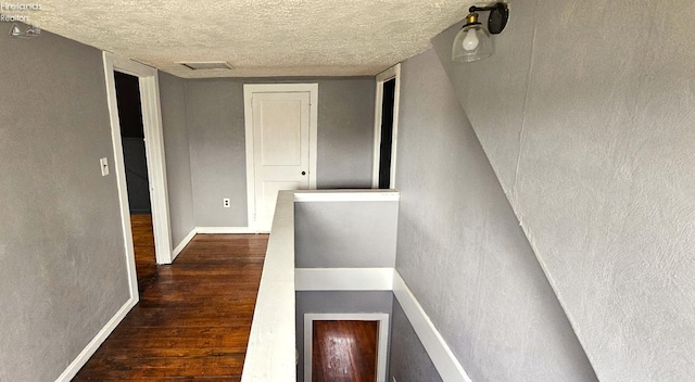 hall featuring a textured ceiling, dark wood-style flooring, and baseboards