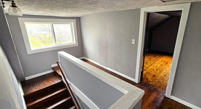 stairway with a textured ceiling, baseboards, and wood-type flooring