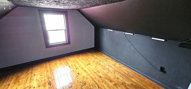 additional living space featuring baseboards, hardwood / wood-style flooring, and vaulted ceiling